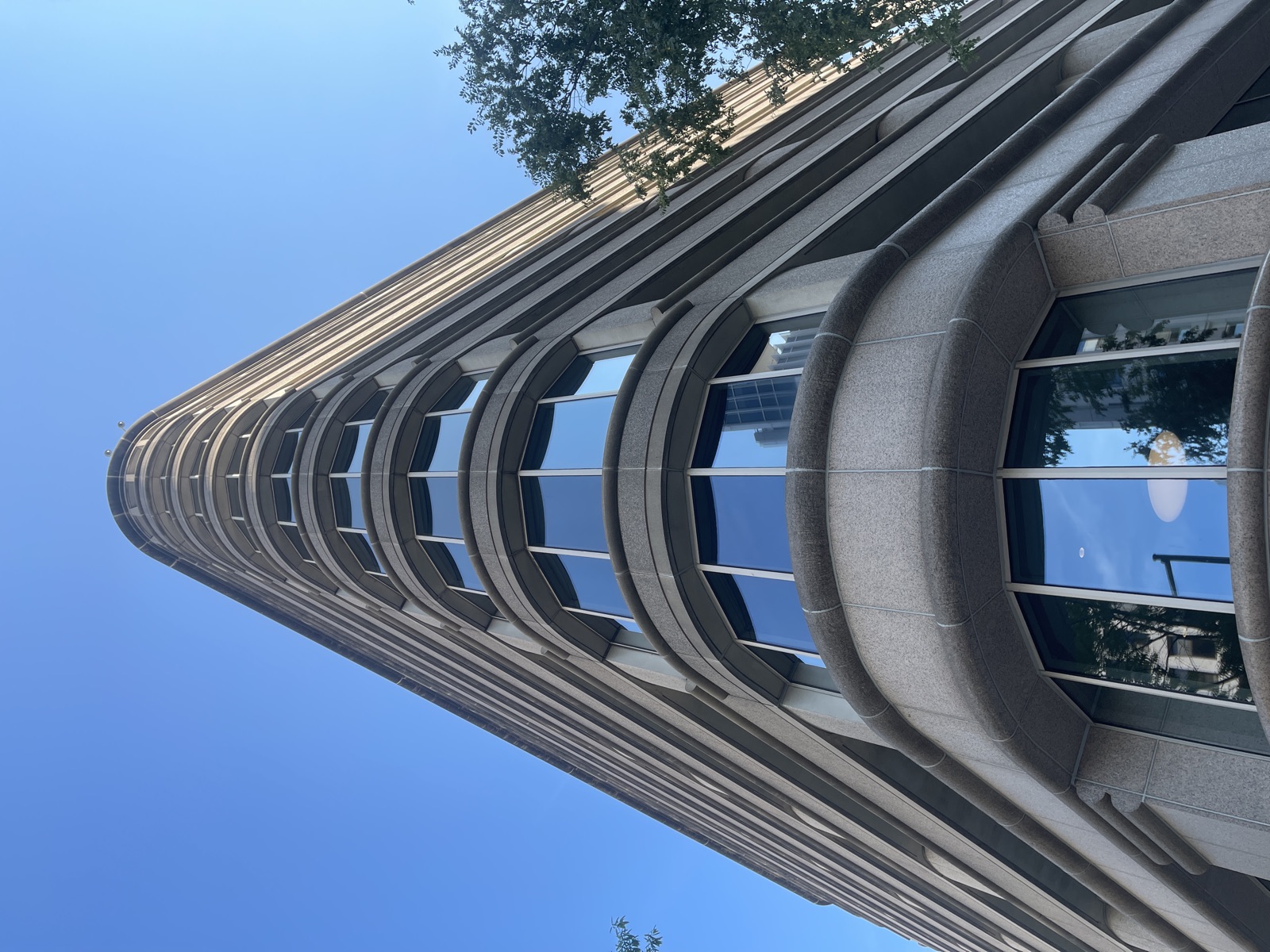 Looking straight up the curved granite prow of a high-rise against blue sky