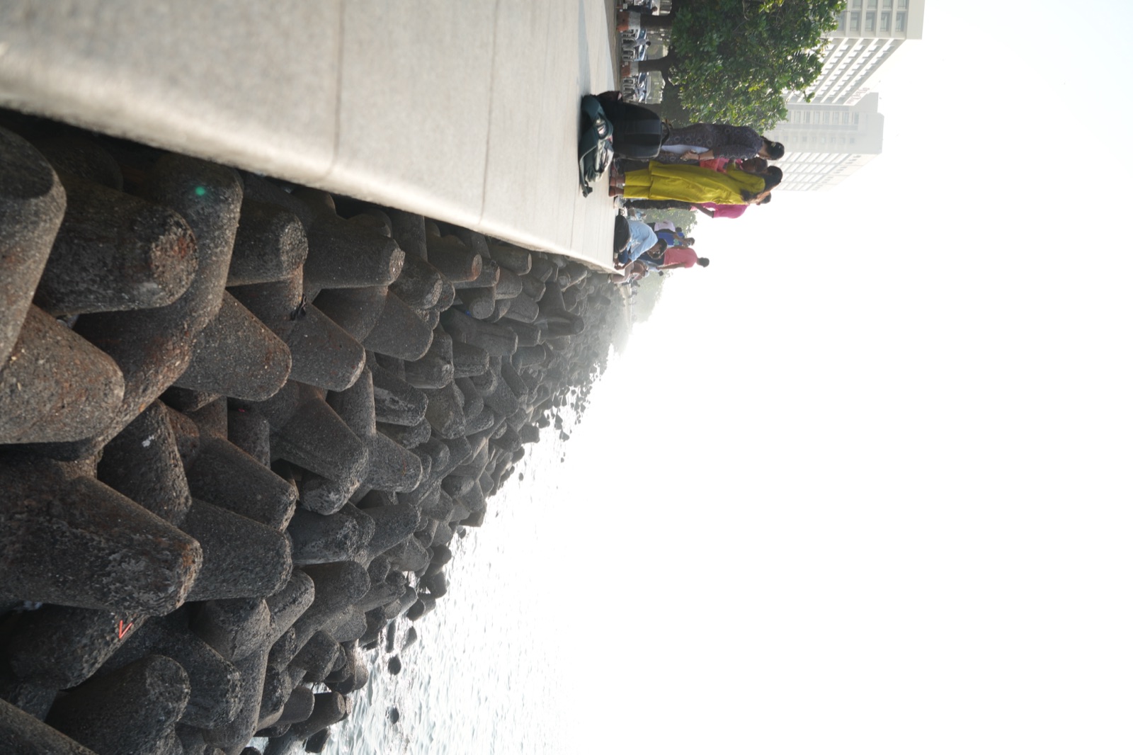 People gathered on Marine Drive promenade above concrete tetrapods fading into sea haze