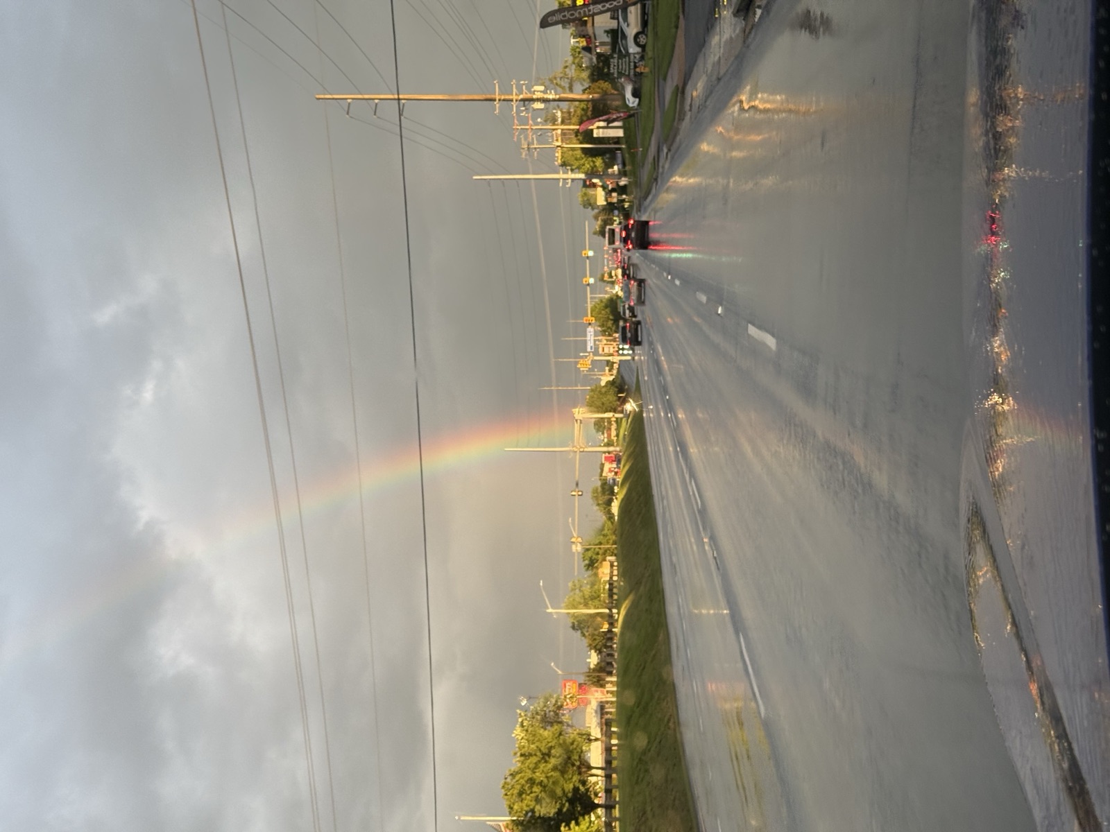 Rainbow rising from a rain-soaked suburban road under heavy gray clouds