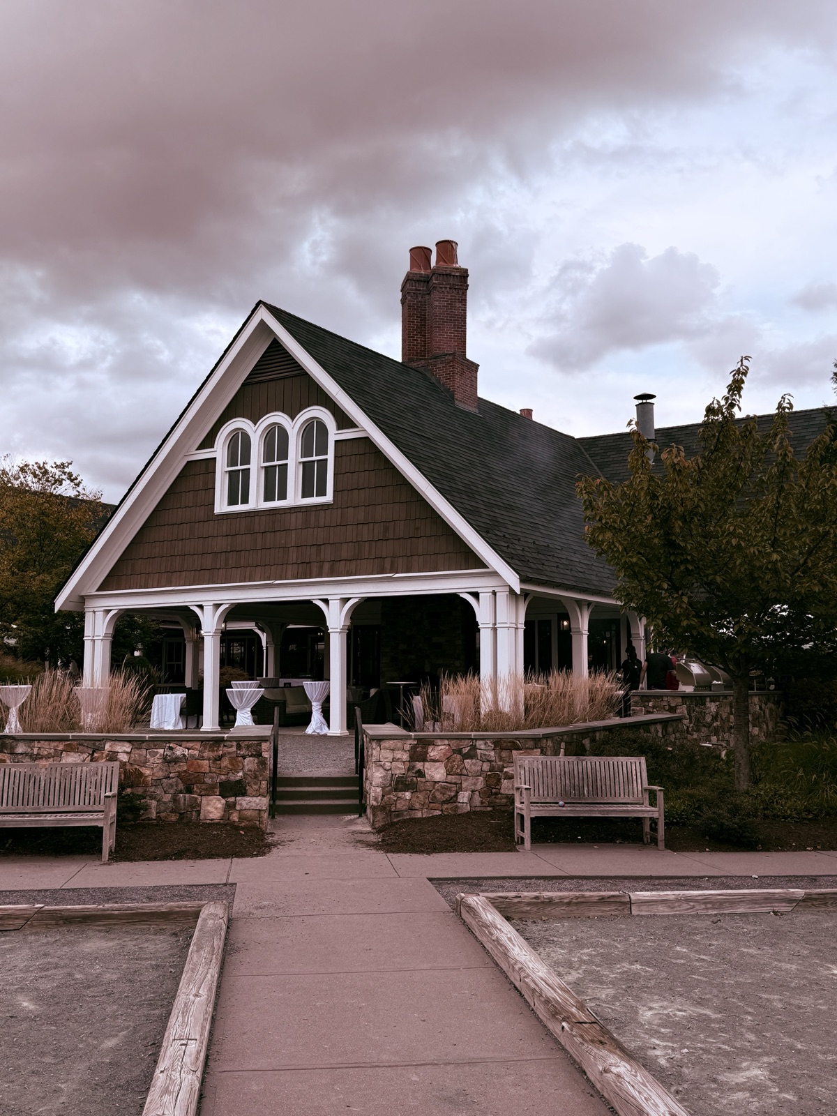 Shingled clubhouse with arched windows and stone terrace under a moody pink evening sky
