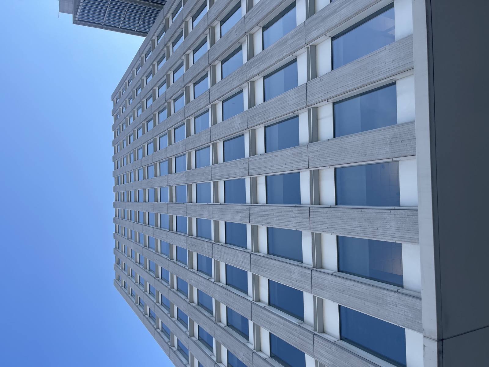 Upward view of a gridded gray stone office tower against clear blue sky
