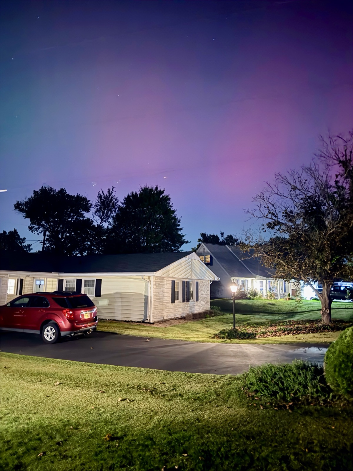Faint purple aurora over a suburban house and red Chevrolet Equinox at night