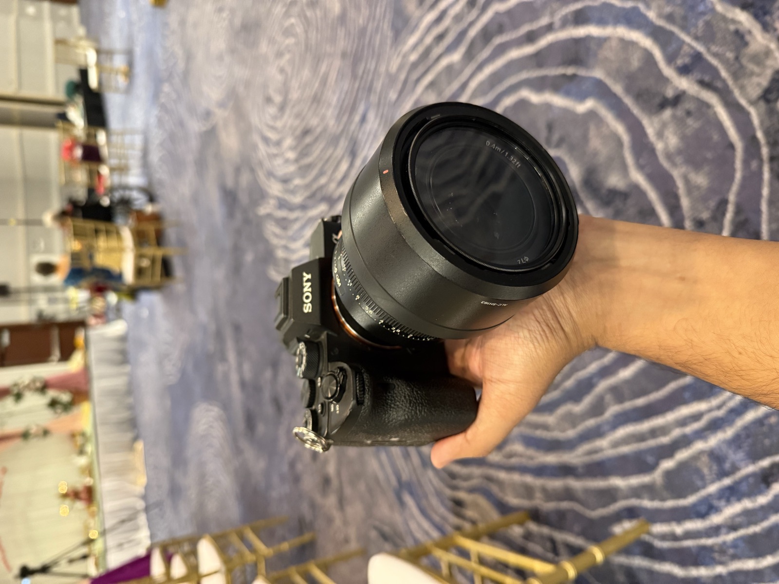 Hand holding a Sony mirrorless camera with large lens in an empty wedding ballroom