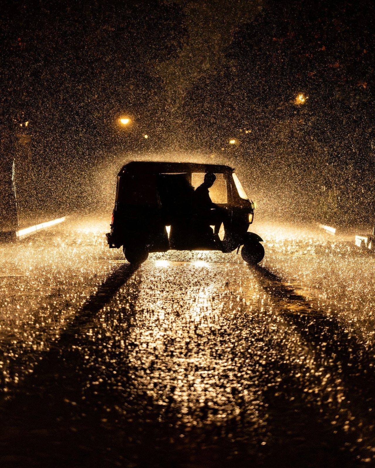 Auto-rickshaw silhouetted against backlit heavy night rain on a glistening road