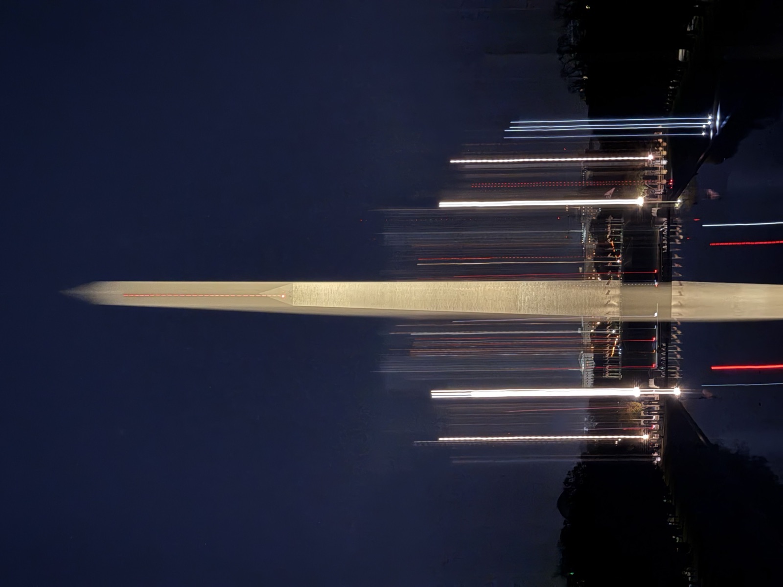 Washington Monument at night with streaked flag lights mirrored in the reflecting pool