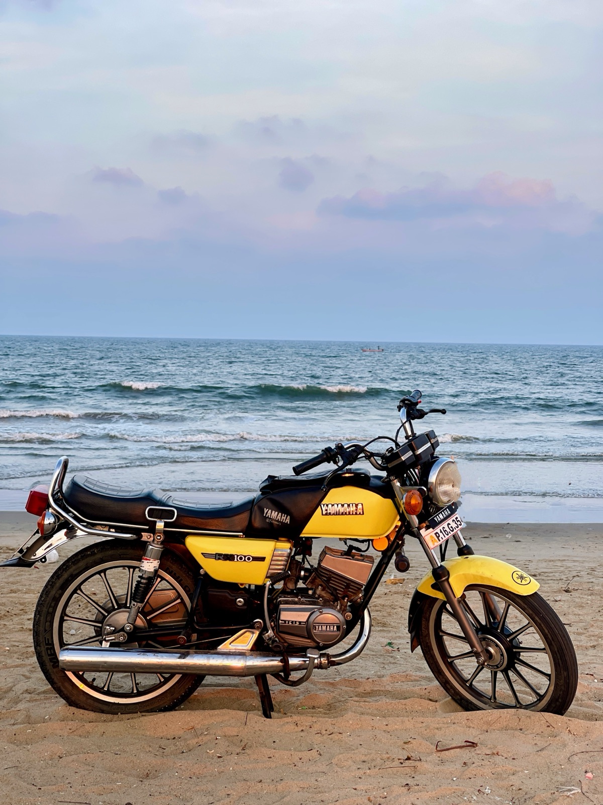 Yellow Yamaha RX100 motorcycle parked on beach sand before evening surf